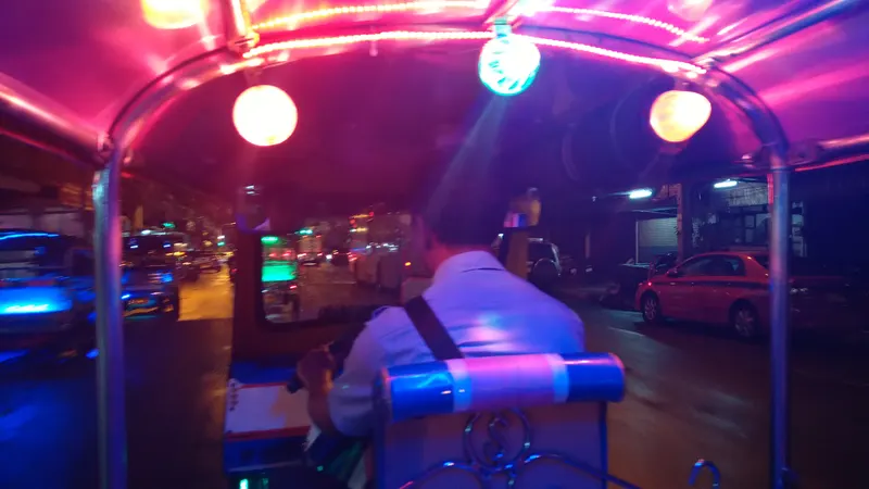 View from a tuk-tuk on a neon-lit Bangkok street at night